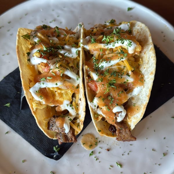 Two steak tacos with cheese, salsa, and sour cream on a white plate with a black napkin.