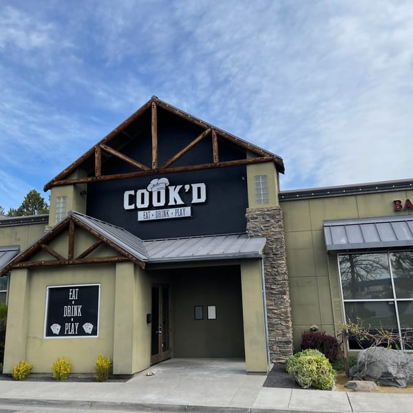The exterior of Cook'd restaurant, featuring a rustic design with wooden beams and stone accents.