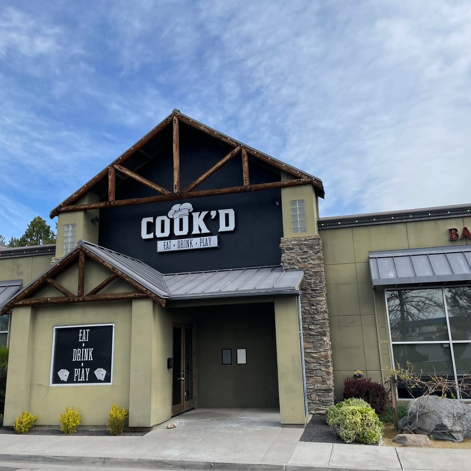 The exterior of Cook'd restaurant, featuring a rustic design with wooden beams and stone accents.