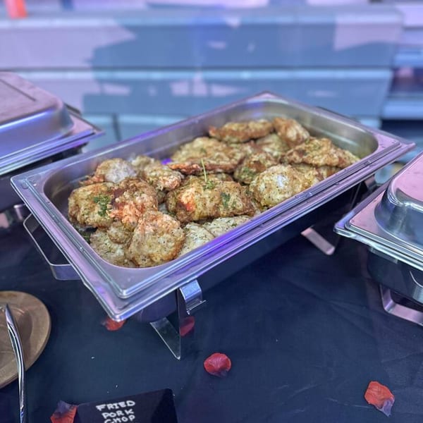 A stainless steel chafing dish filled with fried pork chops on a black tablecloth.