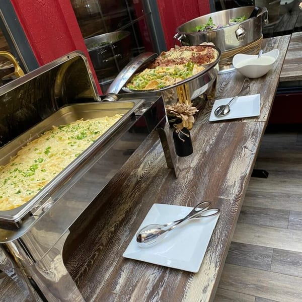 Buffet table with Cook'd pasta dishes, salad, and serving utensils in chafing dishes.
