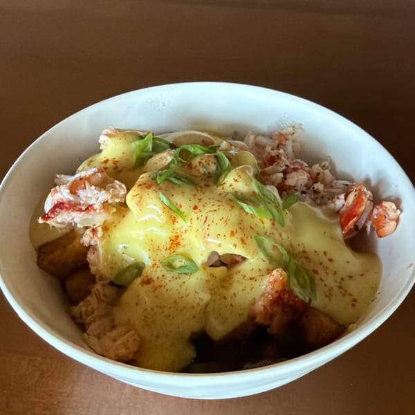 Lobster poutine with golden cheese sauce, green onions, and paprika in a white bowl.