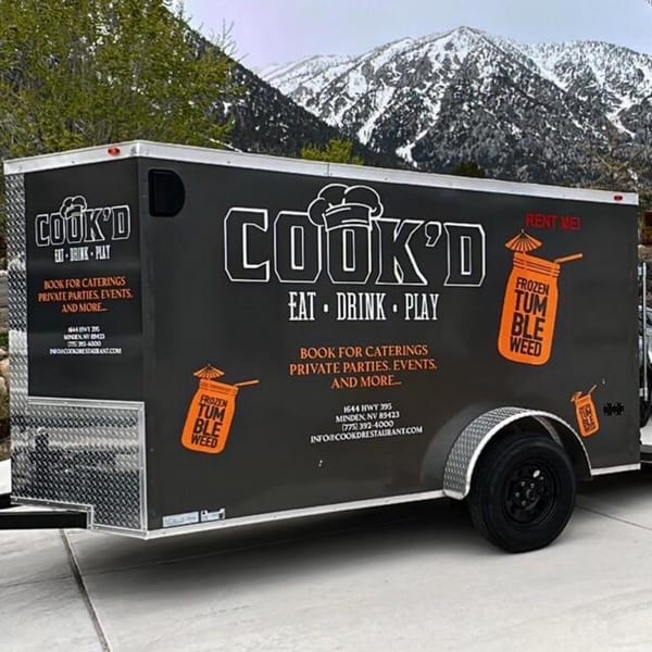 Cook'd food truck trailer with branding, contact info, and snowy mountains in the background.