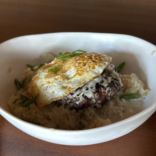 Loco Moco with a fried egg, hamburger patty, gravy, and rice, garnished with green onions.
