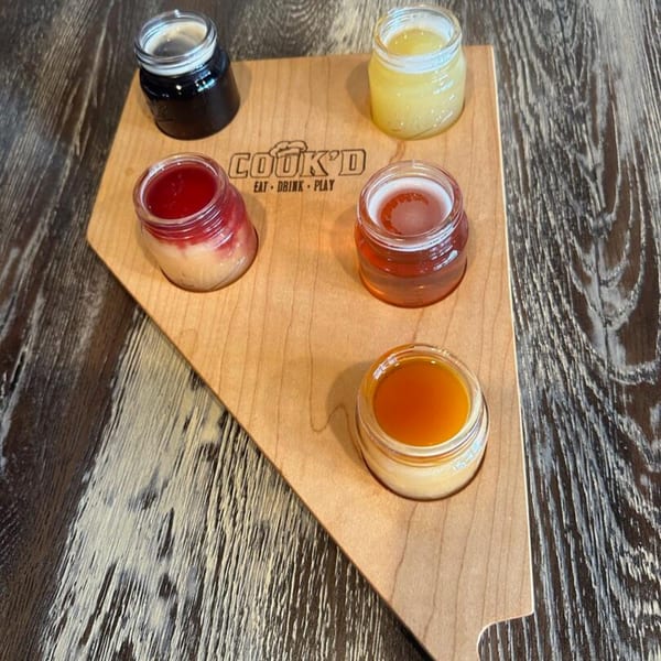 A pizza-slice shaped wooden board with five small jars of colorful drinks from Cook'd.