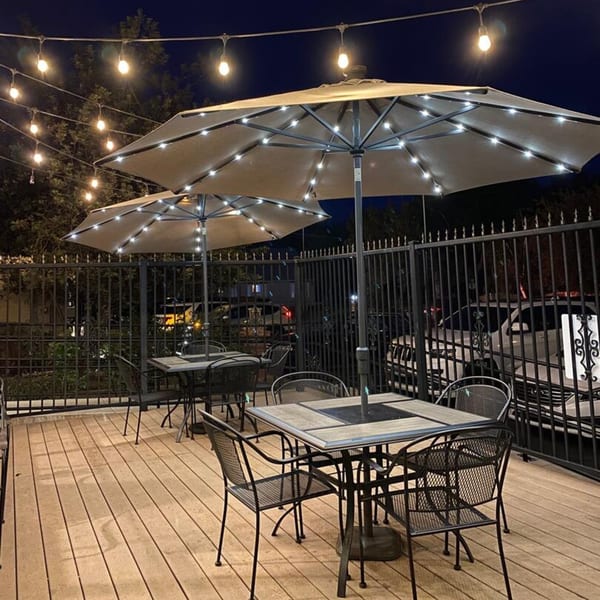 Cook'd outdoor patio at night with illuminated umbrellas, string lights, and empty tables.