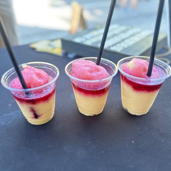 Three layered frozen drinks with yellow, red, and pink layers, each with a black straw.