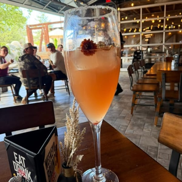 A tall glass of pink cocktail with a flower garnish on a table in a restaurant.