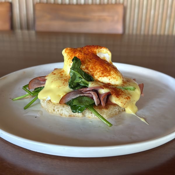 Eggs Benedict with hollandaise sauce, spinach, and ham on toast, dusted with paprika.