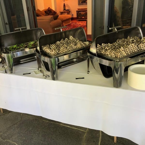 Three Cook'd buffet chafing dishes on a white-clothed table, one with salad, two with wrapped items.