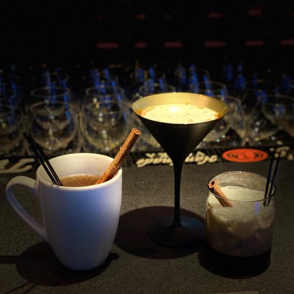 Three festive cocktails, including a hot drink, a martini, and a rocks glass, on a dark bar.