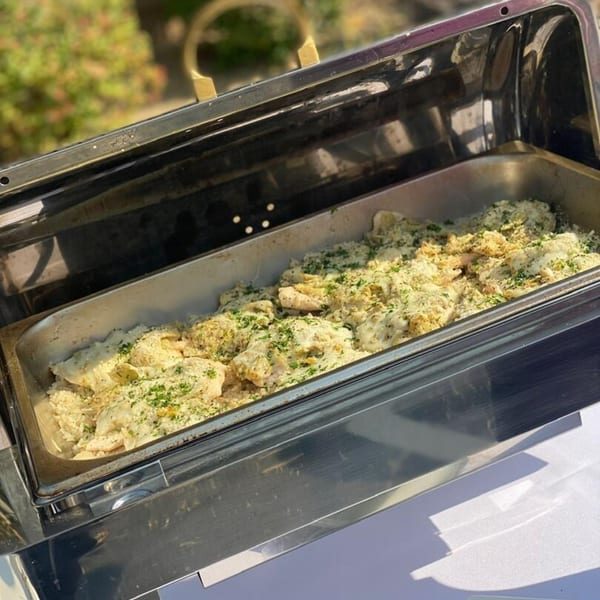 A catering tray filled with creamy pasta topped with cheese and green herbs, ready to be served.