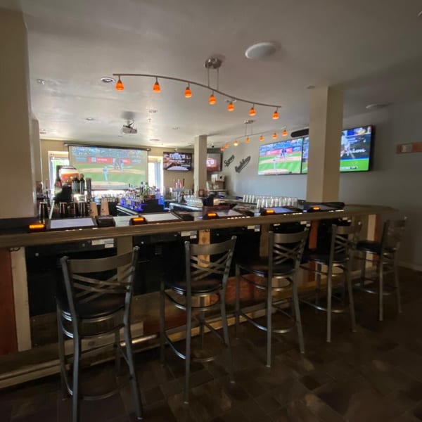 Cook'd restaurant bar area with multiple TVs showing sports, bar stools, and bottles of liquor.