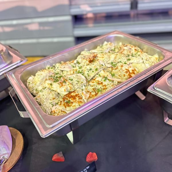 A large metal serving tray filled with baked pasta topped with cheese and herbs.