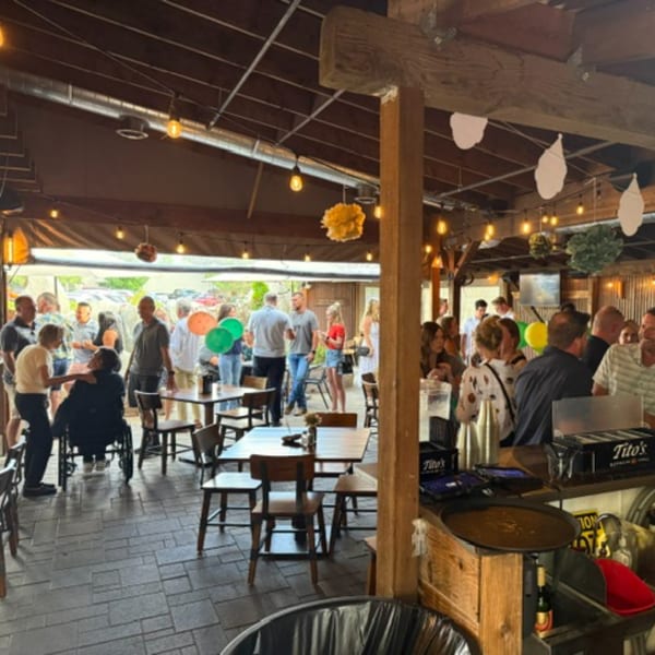 A lively outdoor patio with many people mingling, string lights, and wooden tables.