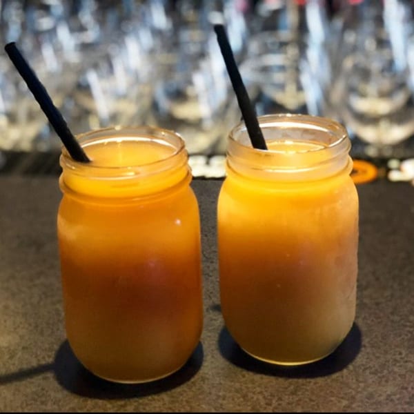 Two mason jar glasses filled with orange drinks and black straws on a dark countertop.