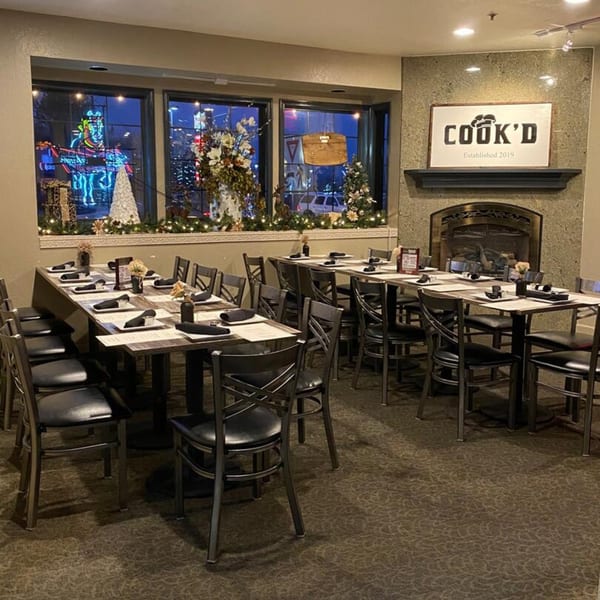 Cook'd restaurant dining room with set tables, a fireplace, and festive window decorations.