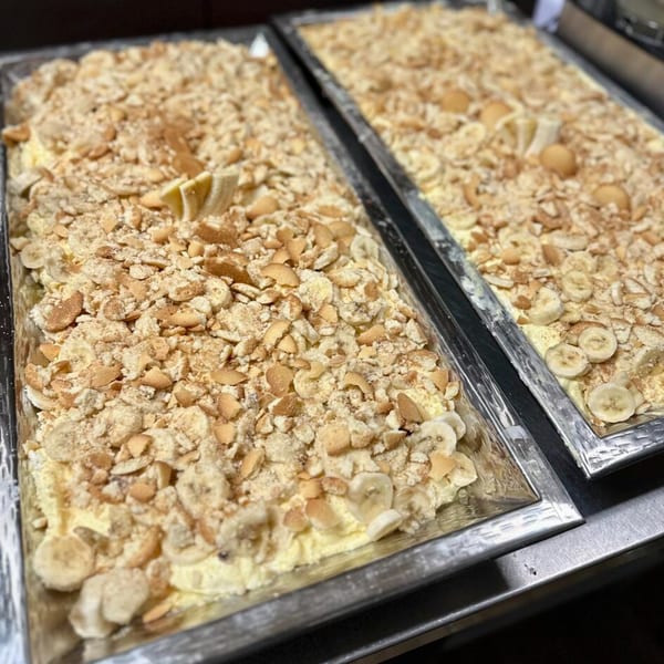 Two large trays of banana pudding topped with crushed vanilla wafers and banana slices.