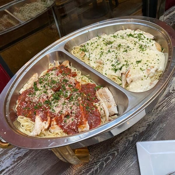 Two chafing dishes of pasta with chicken, one with red sauce and one with white sauce.