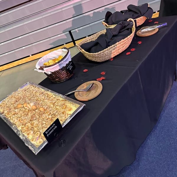 A buffet table with a large tray of banana pudding, baskets of bread, and serving utensils.
