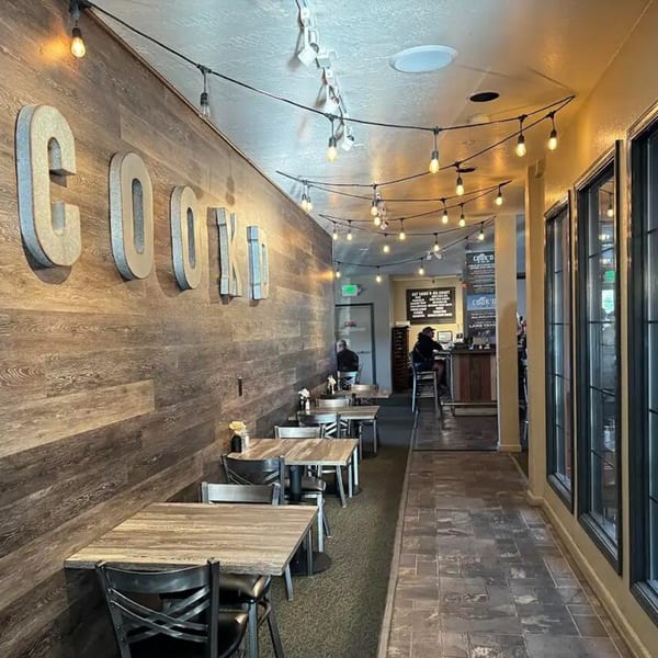 Cook'd restaurant interior with wood-paneled walls, string lights, and empty dining tables.