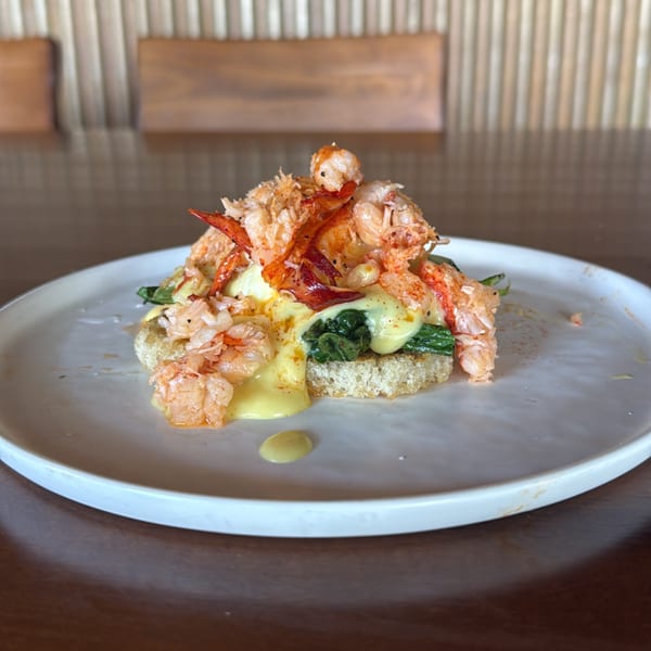 Lobster Benedict with hollandaise sauce and spinach on a white plate, on a wooden table.