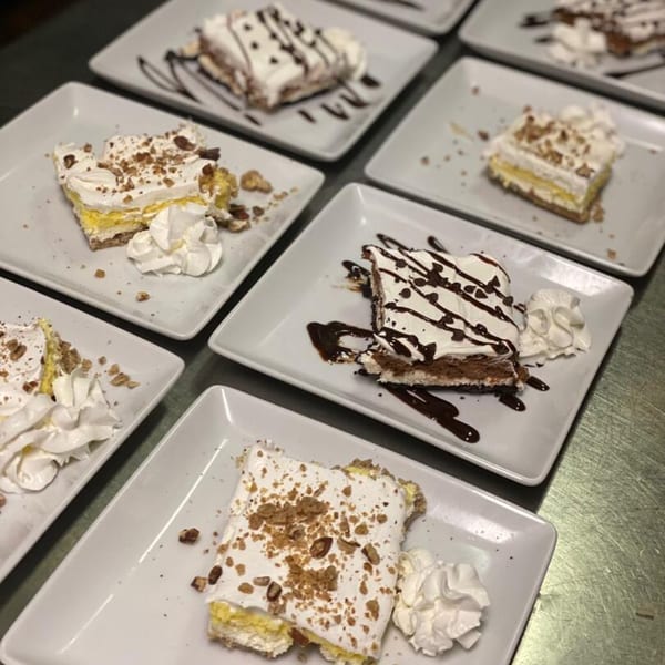 Multiple dessert slices on white plates, some with chocolate drizzle, others with nuts and whipped cream.