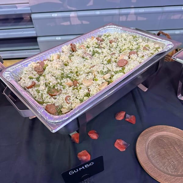 A large catering pan of Cook'd gumbo with rice, sausage, and shrimp, on a black tablecloth.