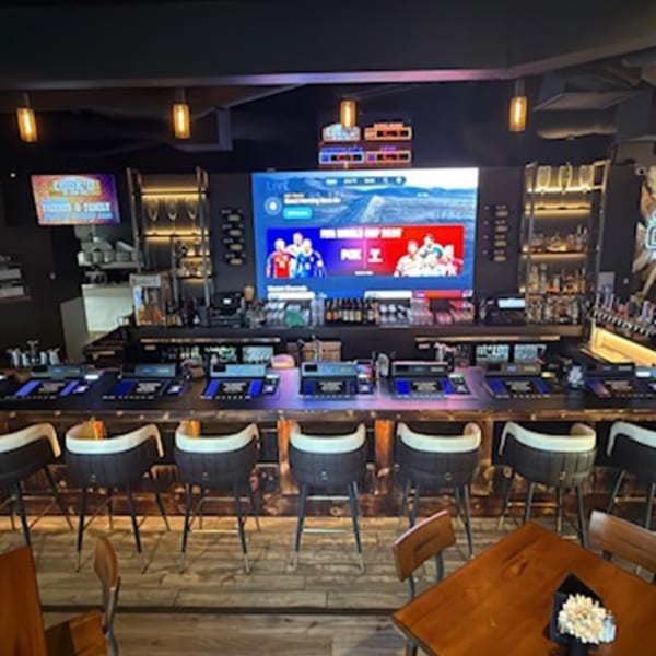 A sports bar with a large screen showing a soccer game, bar stools, and tables.